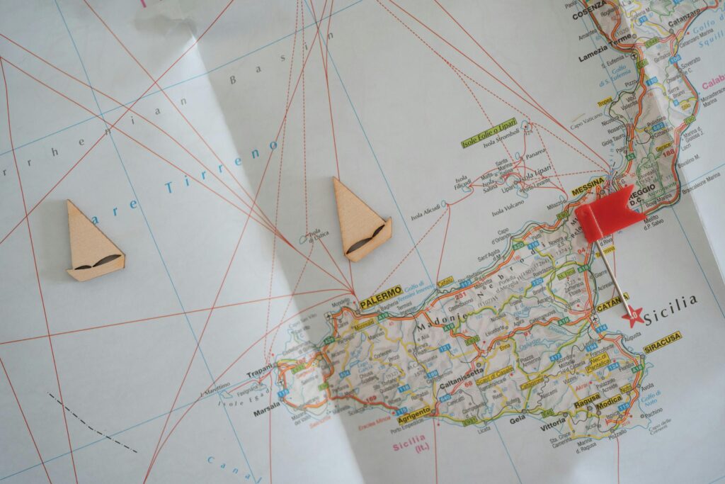 Travel planning concept featuring a Sicily map with wooden boat markers and a red pin.